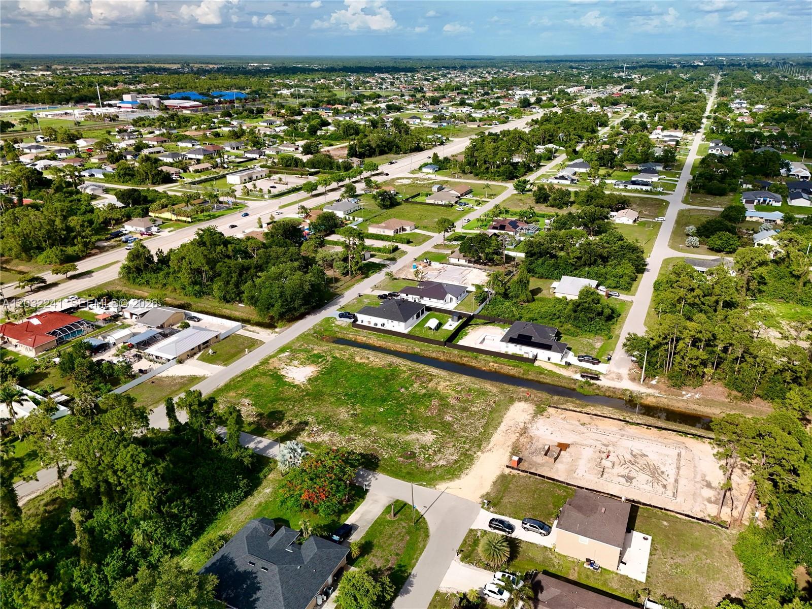 An aerial view shows a suburban neighborhood with houses, vacant lots, and a drainage canal — 0 4th St W, Lehigh Acres FL 33971, LEHIGH ACRES, FL
