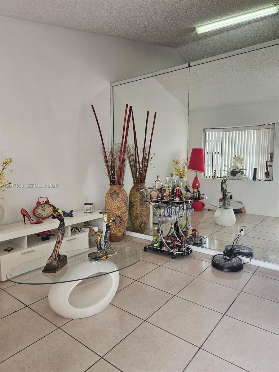 A living room features tiled floors, a mirrored wall, a glass coffee table, and decor — 8805 NW 113th St, Hialeah Gardens FL 33018, HIALEAH GARDENS, FL