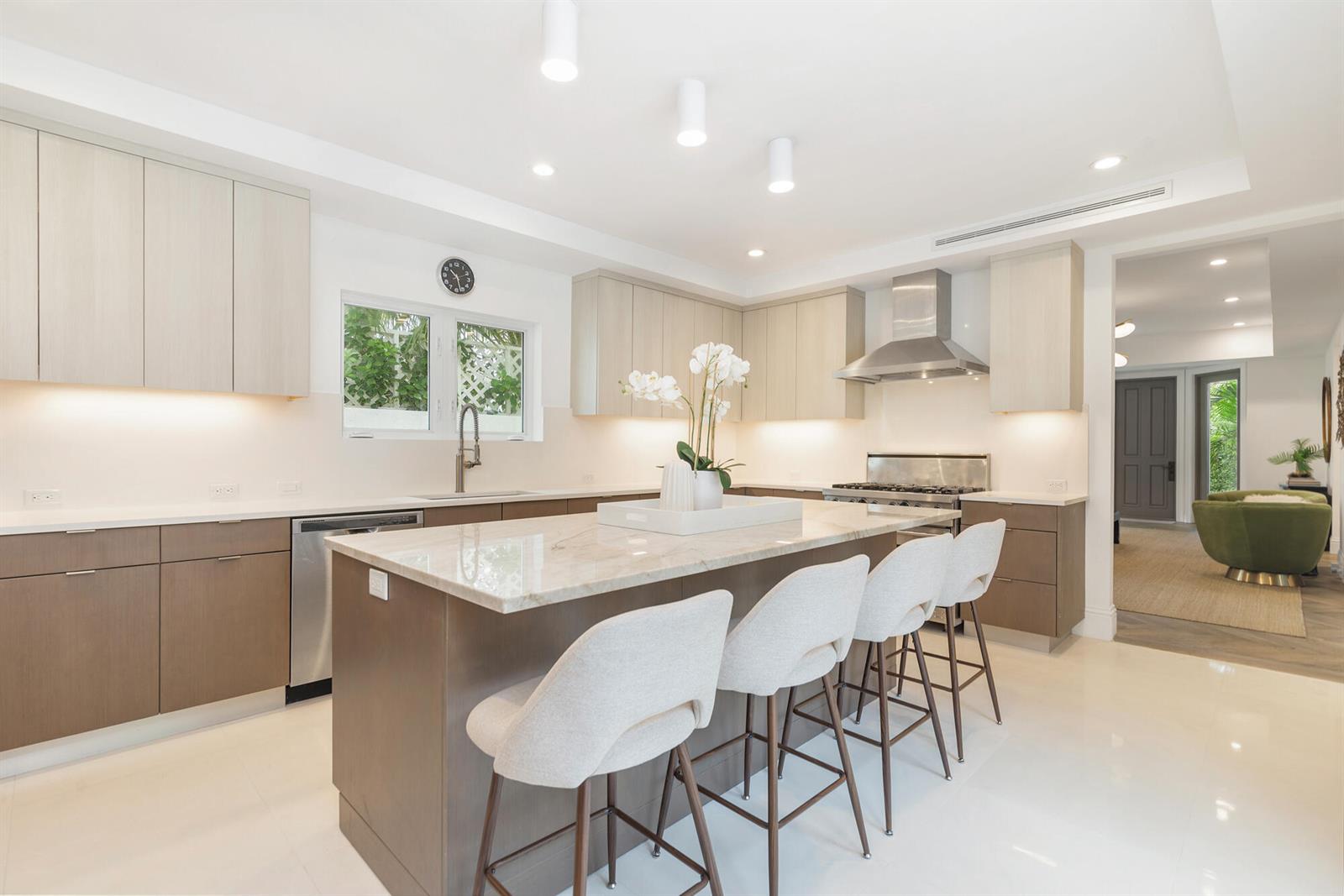 A modern kitchen features light wood cabinetry, a marble-topped island, and four upholstered bar stools — 443 Seaview Avenue, Palm Beach FL 33480, PALM BEACH, FL