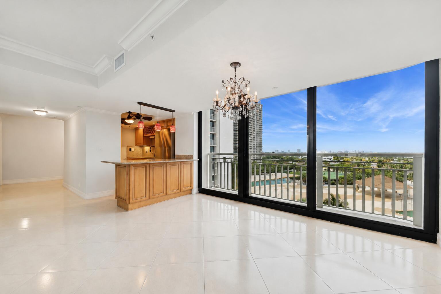 An open dining area with a chandelier, kitchen island, and floor-to-ceiling windows overlooking a city — 3000 N Ocean Drive # A, Singer Island FL 33404, SINGER ISLAND, FL