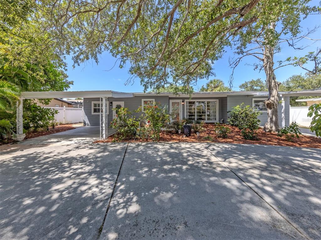 A single-story gray house with a carport and a large concrete driveway under trees — 814 GUILD DRIVE, VENICE, FL