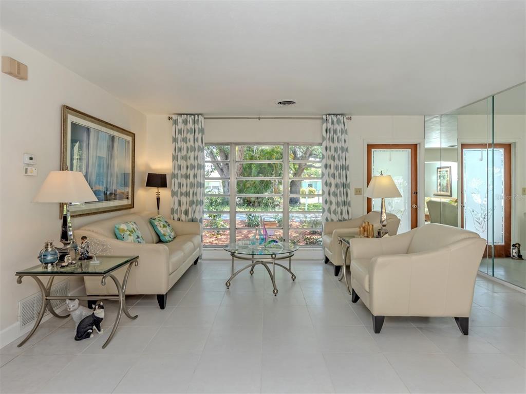 A bright living room features white tile floors, cream-colored furniture, and a large window wall — 814 GUILD DRIVE, VENICE, FL