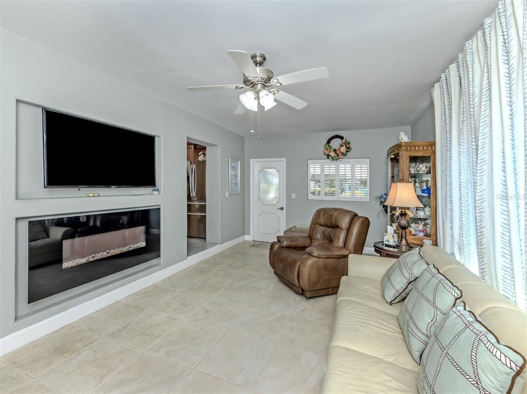 A living room features a wall-mounted television, an electric fireplace, tile flooring, and a recliner — 814 GUILD DRIVE, VENICE, FL