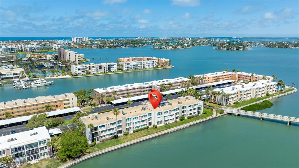 An aerial view shows a multi-story apartment complex situated along a waterfront with a bridge — 7425 BAY ISLAND DRIVE S UNIT 104, SOUTH PASADENA, FL