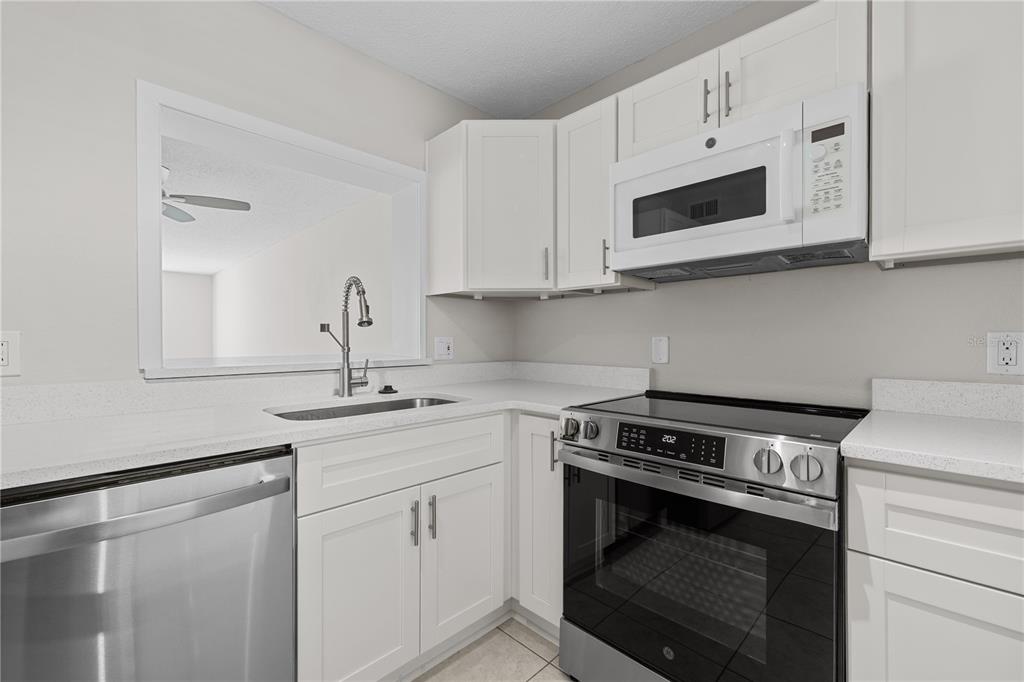 A kitchen features white cabinets, stainless steel appliances, and a pass-through window — 7425 BAY ISLAND DRIVE S UNIT 104, SOUTH PASADENA, FL