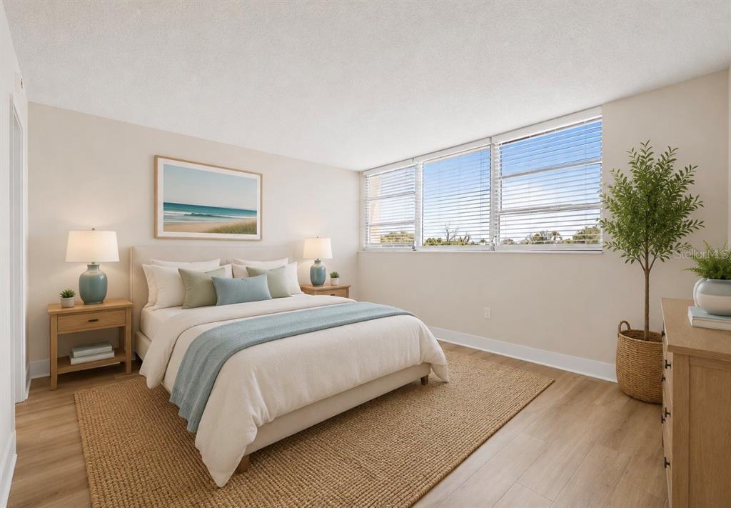 A bedroom features a bed with neutral bedding, two nightstands, a large window, and a plant — 7425 BAY ISLAND DRIVE S UNIT 104, SOUTH PASADENA, FL