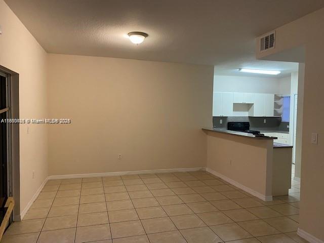 An empty room features beige walls, light-colored tile flooring, vertical window blinds, and a white door — 646 SW 7th Ter, Florida City FL 33034, FLORIDA CITY, FL