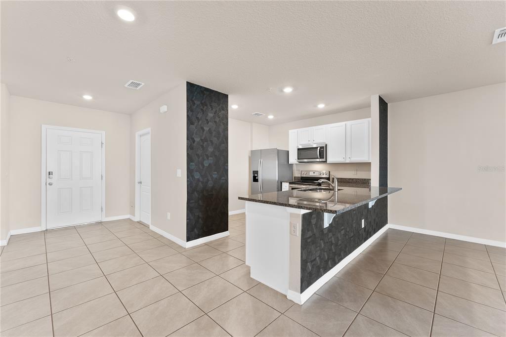 A kitchen with a granite-topped island, white cabinets, and dark geometric accent walls — 12460 BOWES BRANCH ROAD, ORLANDO, FL