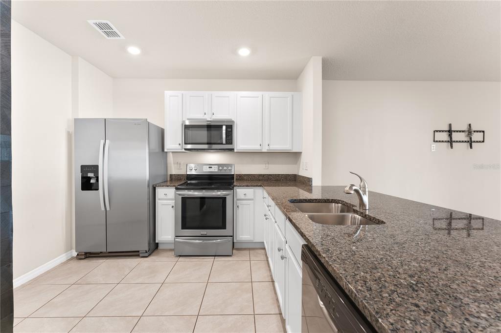 A kitchen features white cabinets, stainless steel appliances, and a granite-topped island with a sink — 12460 BOWES BRANCH ROAD, ORLANDO, FL