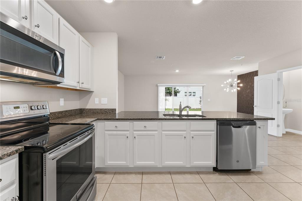 A kitchen with white cabinets, dark granite countertops, stainless steel appliances, and tile flooring — 12460 BOWES BRANCH ROAD, ORLANDO, FL