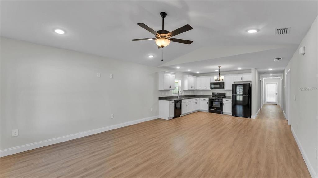 An open-concept living area features light wood-look flooring, white cabinets, and black kitchen appliances — 1246 DOROTHY STREET, LAKELAND, FL
