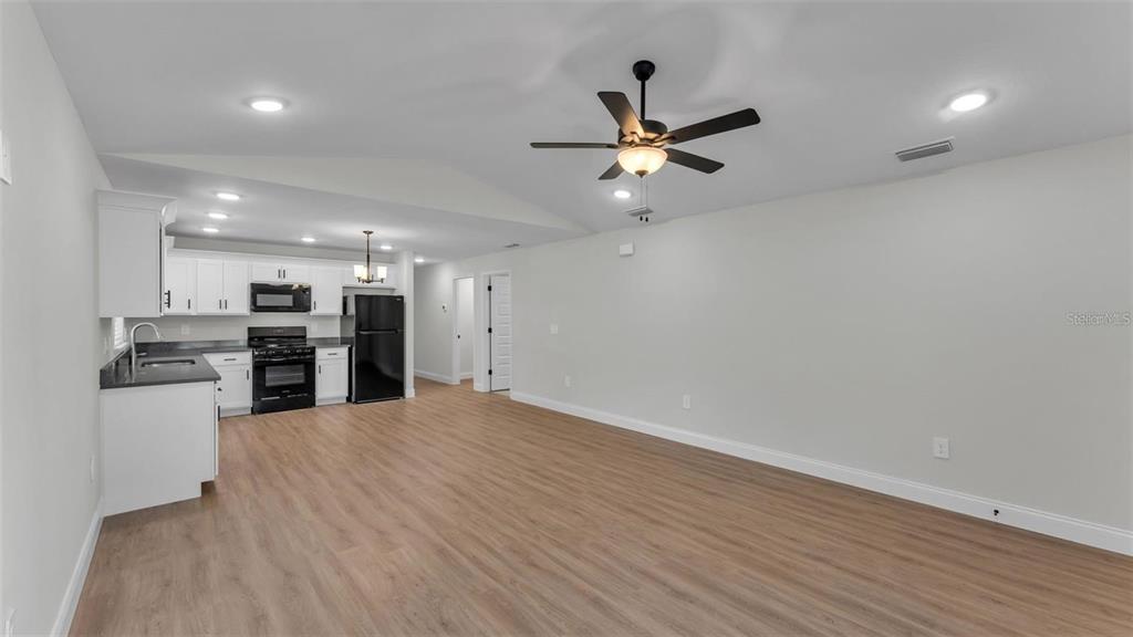 An open-concept kitchen and living area with white cabinets, black appliances, and wood-look flooring — 1246 DOROTHY STREET, LAKELAND, FL
