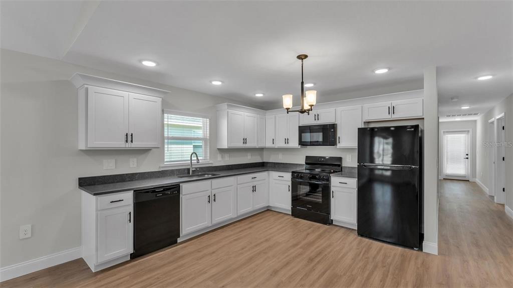 A kitchen with white cabinets, black appliances, dark countertops, and light wood-look flooring — 1246 DOROTHY STREET, LAKELAND, FL