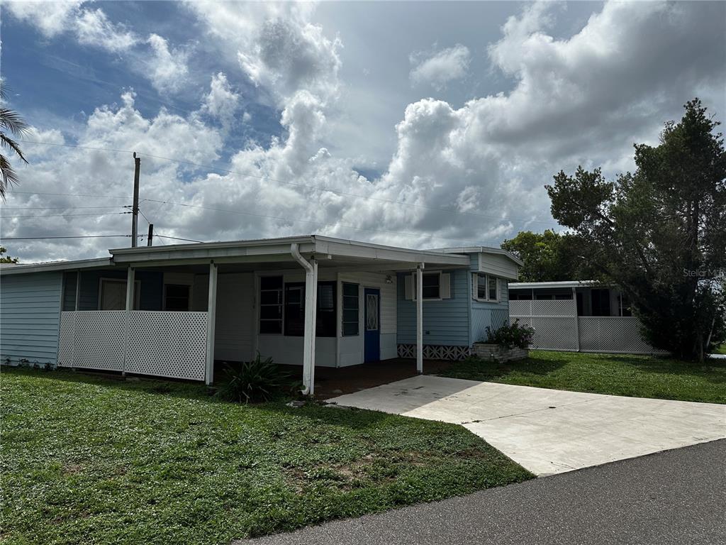 A light blue mobile home features a covered carport, a concrete driveway, and white lattice skirting — 324 TRAILORAMA DRIVE, NORTH PORT, FL