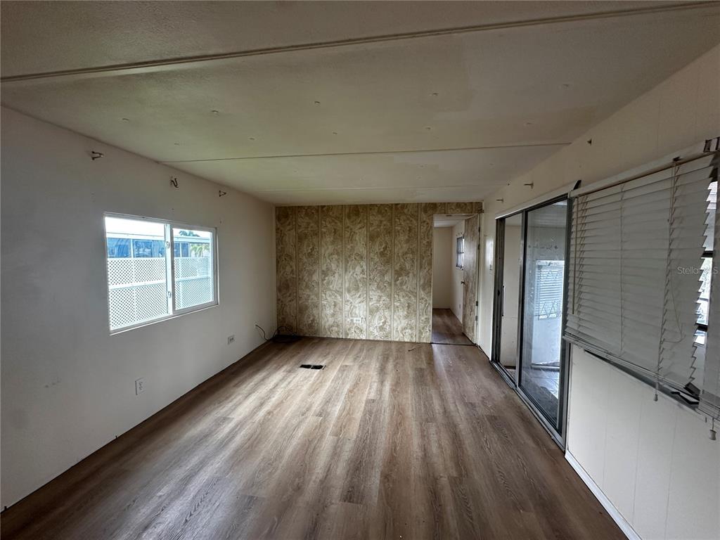 An empty living room features wood-look flooring, a patterned accent wall, and sliding glass doors — 324 TRAILORAMA DRIVE, NORTH PORT, FL
