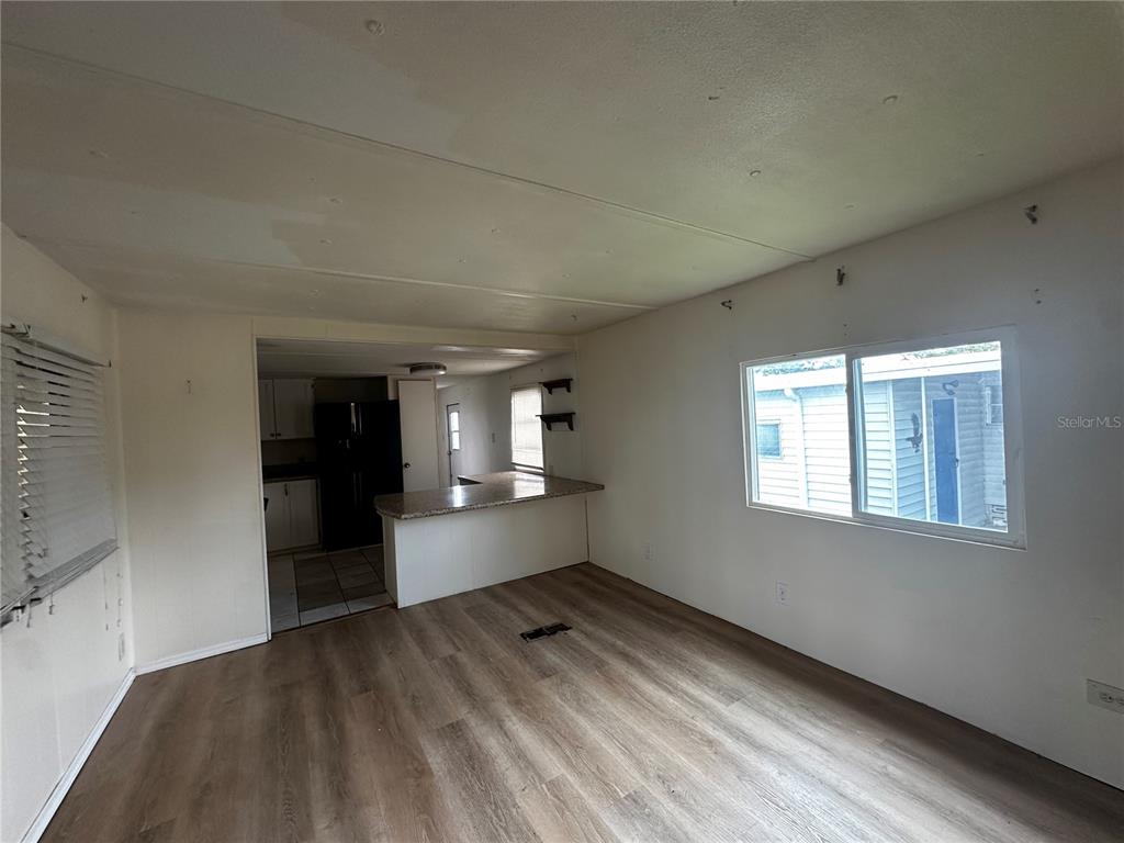 An interior view shows a living room with wood-look flooring leading to a kitchen area — 324 TRAILORAMA DRIVE, NORTH PORT, FL