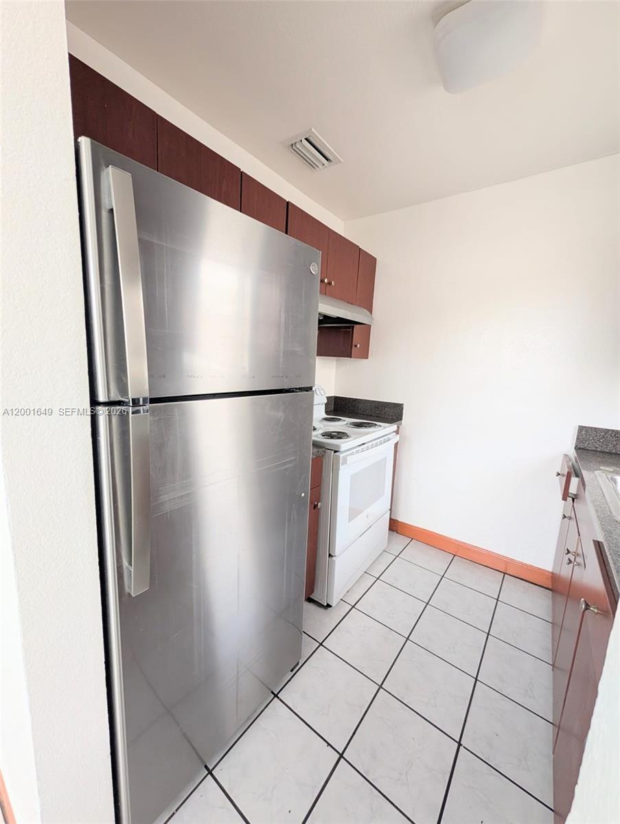 A narrow kitchen features a stainless steel refrigerator, white electric stove, and dark wood cabinets — 1551 NE 8th St # 8, Homestead FL 33033, HOMESTEAD, FL