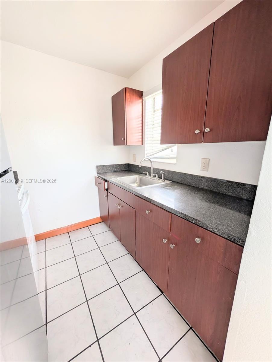 A kitchen features dark wood cabinets, a granite countertop, a sink, and white tiled floors — 1551 NE 8th St # 8, Homestead FL 33033, HOMESTEAD, FL