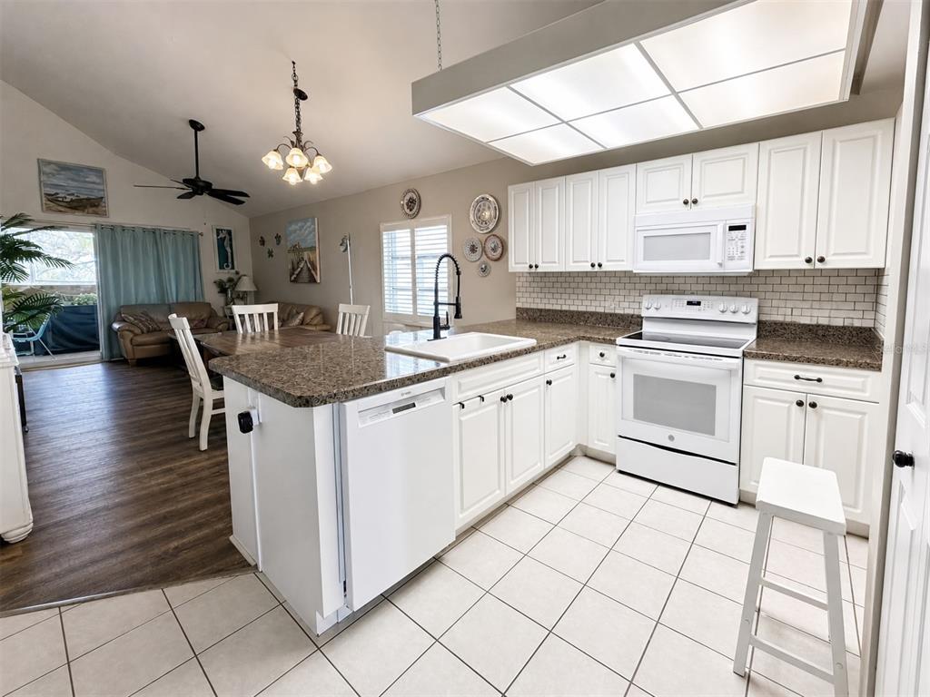 A kitchen features white cabinets, granite countertops, a tile backsplash, and an adjacent dining area — 6800 PLACIDA ROAD UNIT 257, ENGLEWOOD, FL