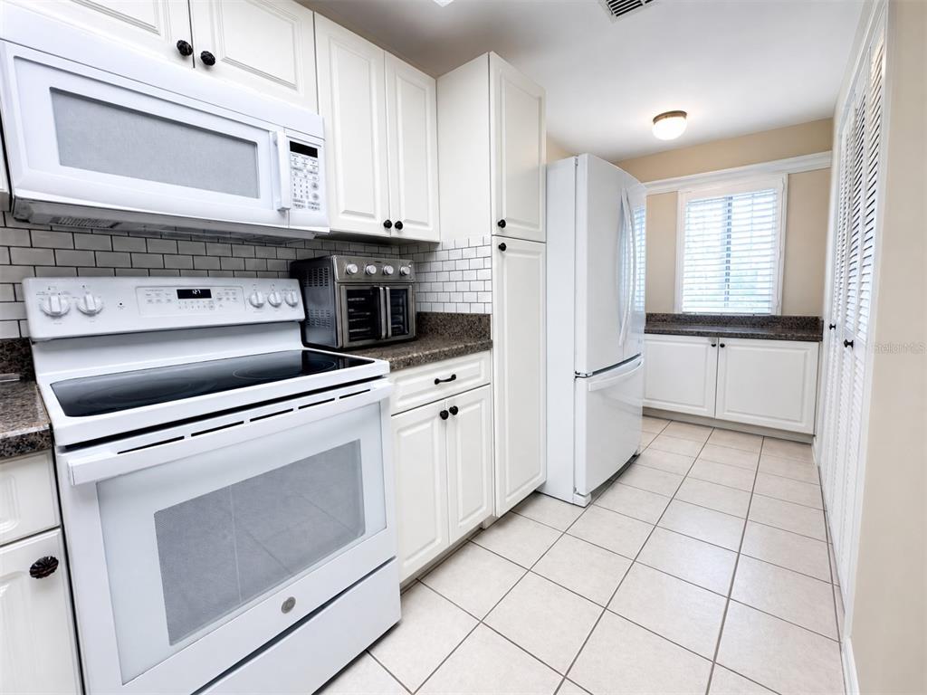 A kitchen features white cabinetry, white appliances, a subway tile backsplash, and tiled flooring — 6800 PLACIDA ROAD UNIT 257, ENGLEWOOD, FL
