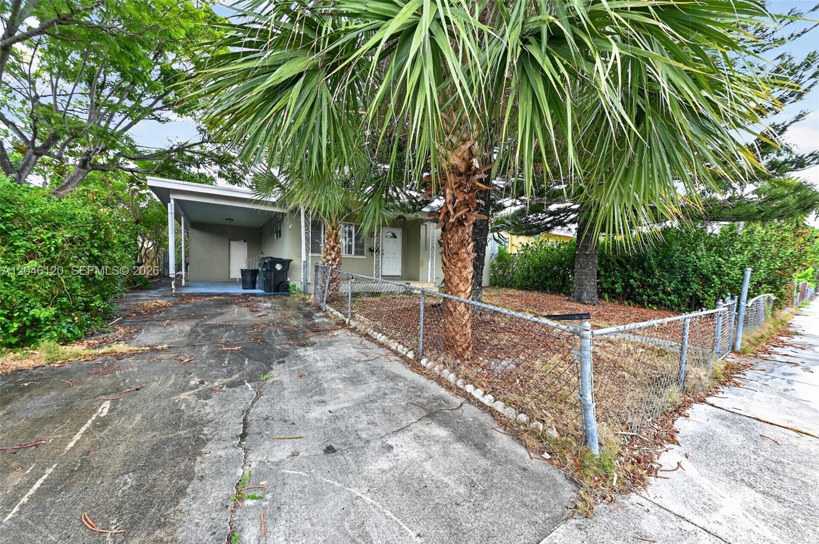 A single-story house with a carport and chain-link fence sits behind palm trees — 914 N K St, Lake Worth FL 33460, LAKE WORTH, FL