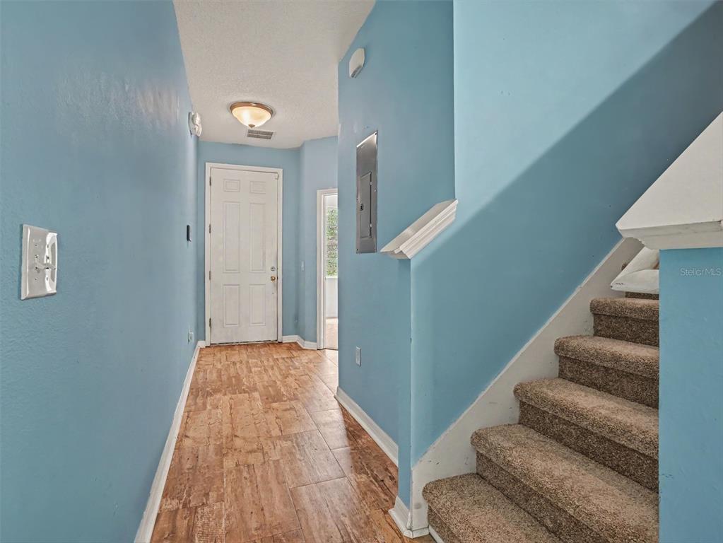 An entryway features light blue walls, wood-look tile flooring, and a carpeted staircase — 7631 LONG ISLAND DR, KISSIMMEE, FL