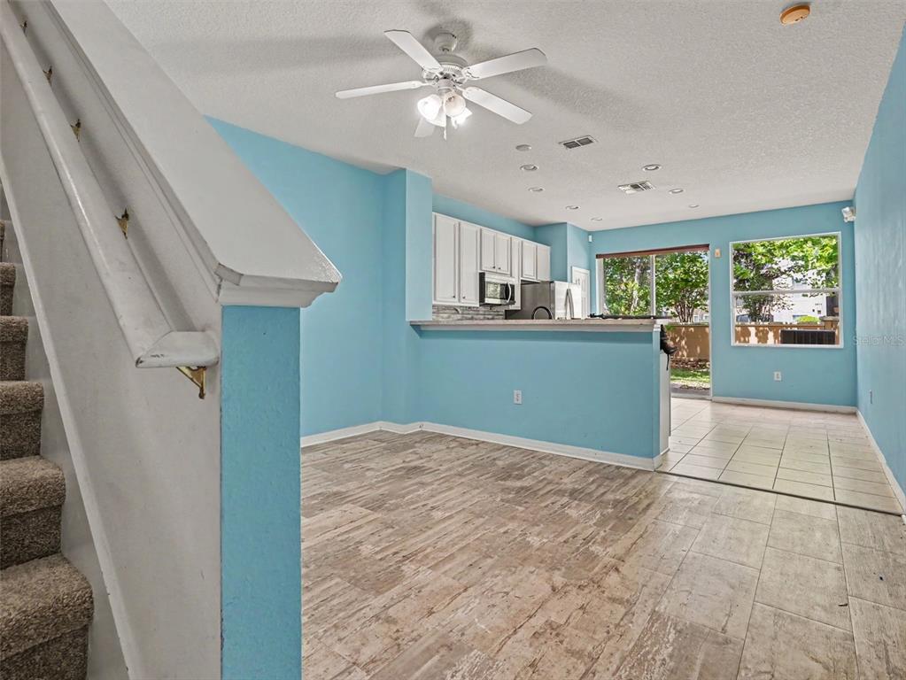 A light blue living area with wood-look tile flooring leads to a kitchen and patio — 7631 LONG ISLAND DR, KISSIMMEE, FL
