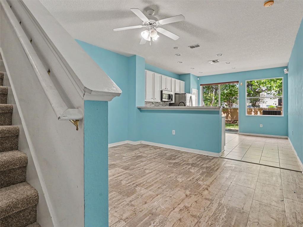 A living area with light blue walls, wood-look flooring, and a staircase leads to a kitchen — 7631 LONG ISLAND DR, KISSIMMEE, FL