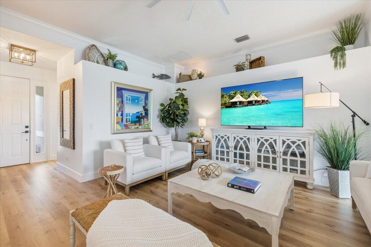A bright living room features white furniture, a large television, and light wood flooring — 6265 33rd Manor, Vero Beach FL 32966, VERO BEACH, FL