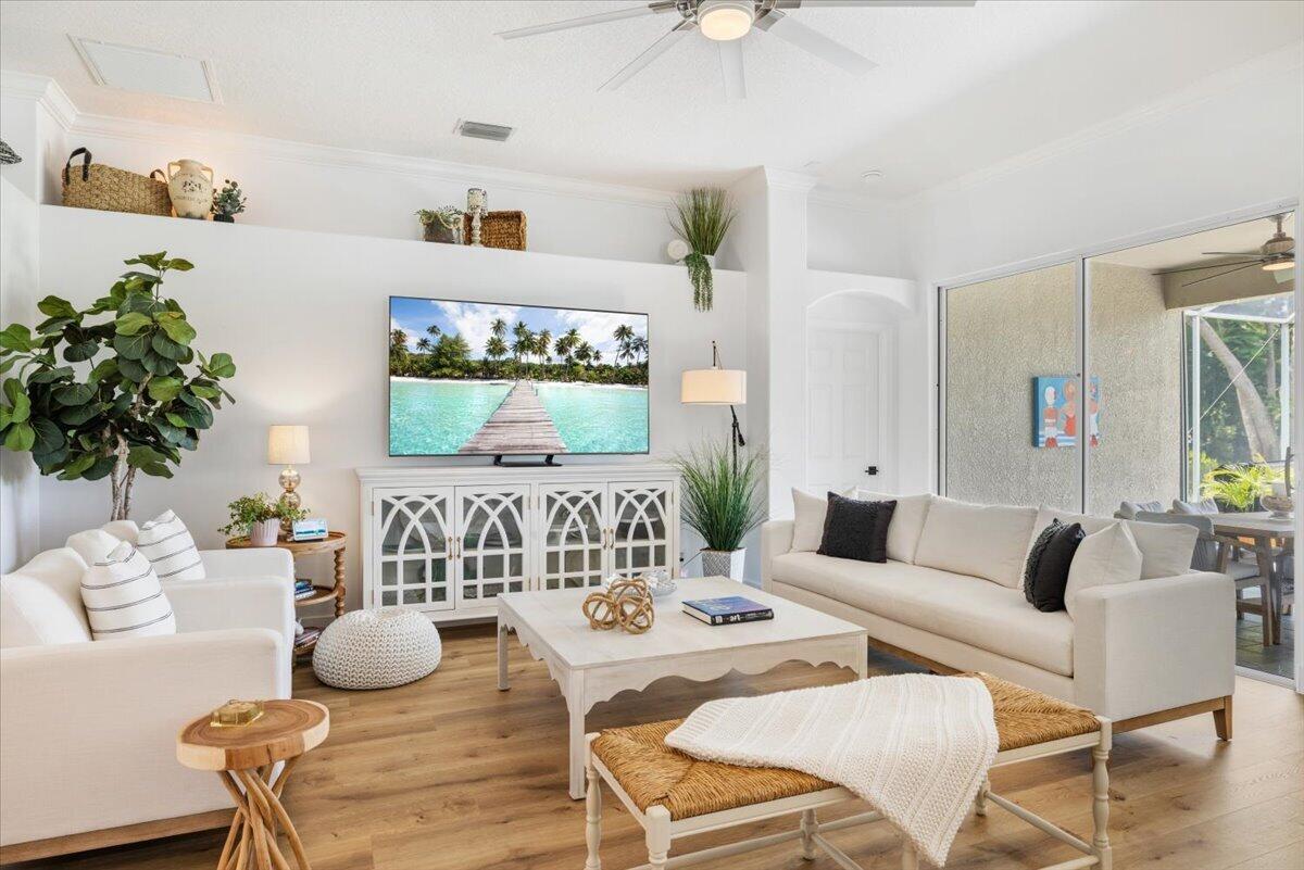 A bright living room features white sofas, a wooden coffee table, and a wall-mounted television — 6265 33rd Manor, Vero Beach FL 32966, VERO BEACH, FL