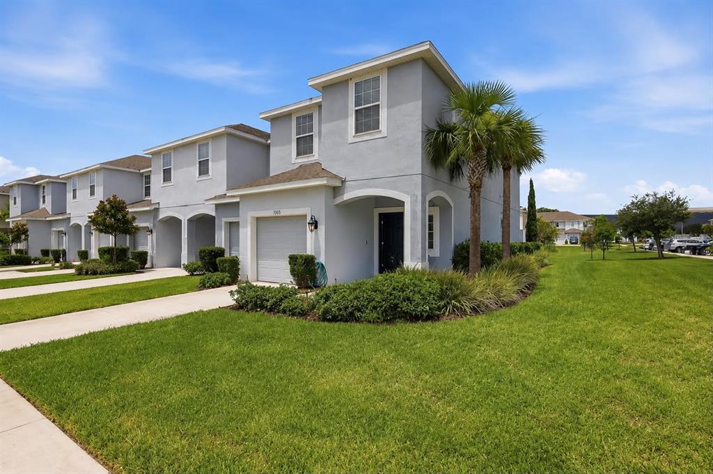 A row of two-story gray townhouses with attached garages and manicured lawns under a blue sky — 7005 GRAND ELM DRIVE, RIVERVIEW, FL