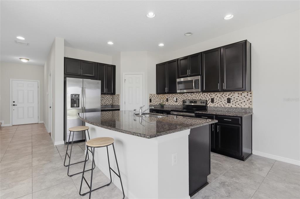 A kitchen features dark wood cabinets, granite countertops, a center island, and stainless steel appliances — 7005 GRAND ELM DRIVE, RIVERVIEW, FL
