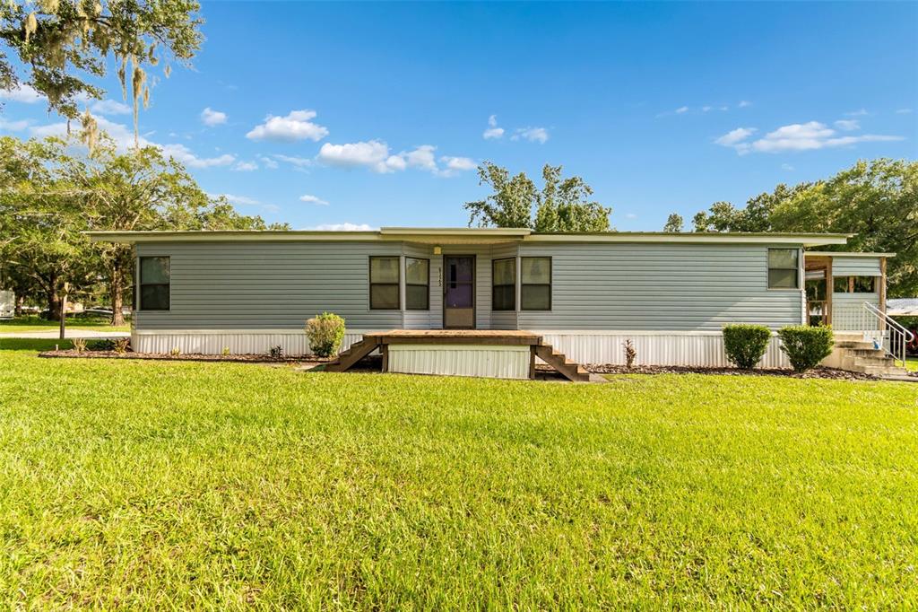 A single-story manufactured home with grey siding and a wooden front deck sits on grass — 6325 OAKVIEW LANE, LAKELAND, FL