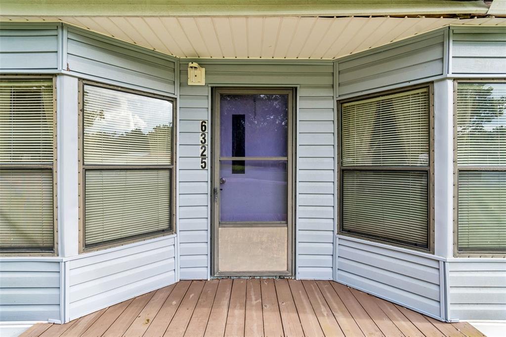 A front porch with a wooden deck leads to a door with a storm screen — 6325 OAKVIEW LANE, LAKELAND, FL