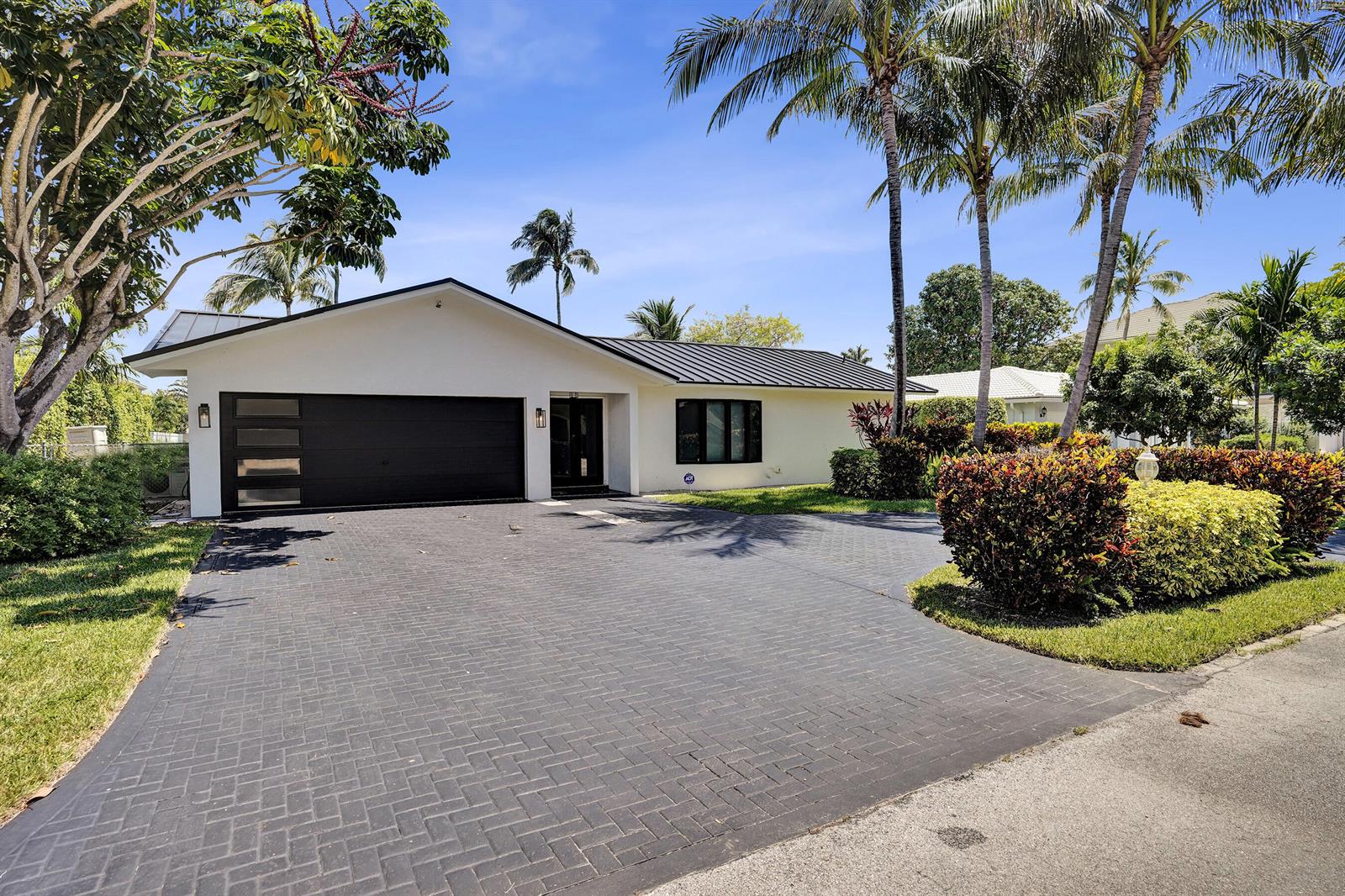 A single-story house with a black metal roof, dark garage door, and paved driveway — 933 Banyan Drive, Delray Beach FL 33483, DELRAY BEACH, FL