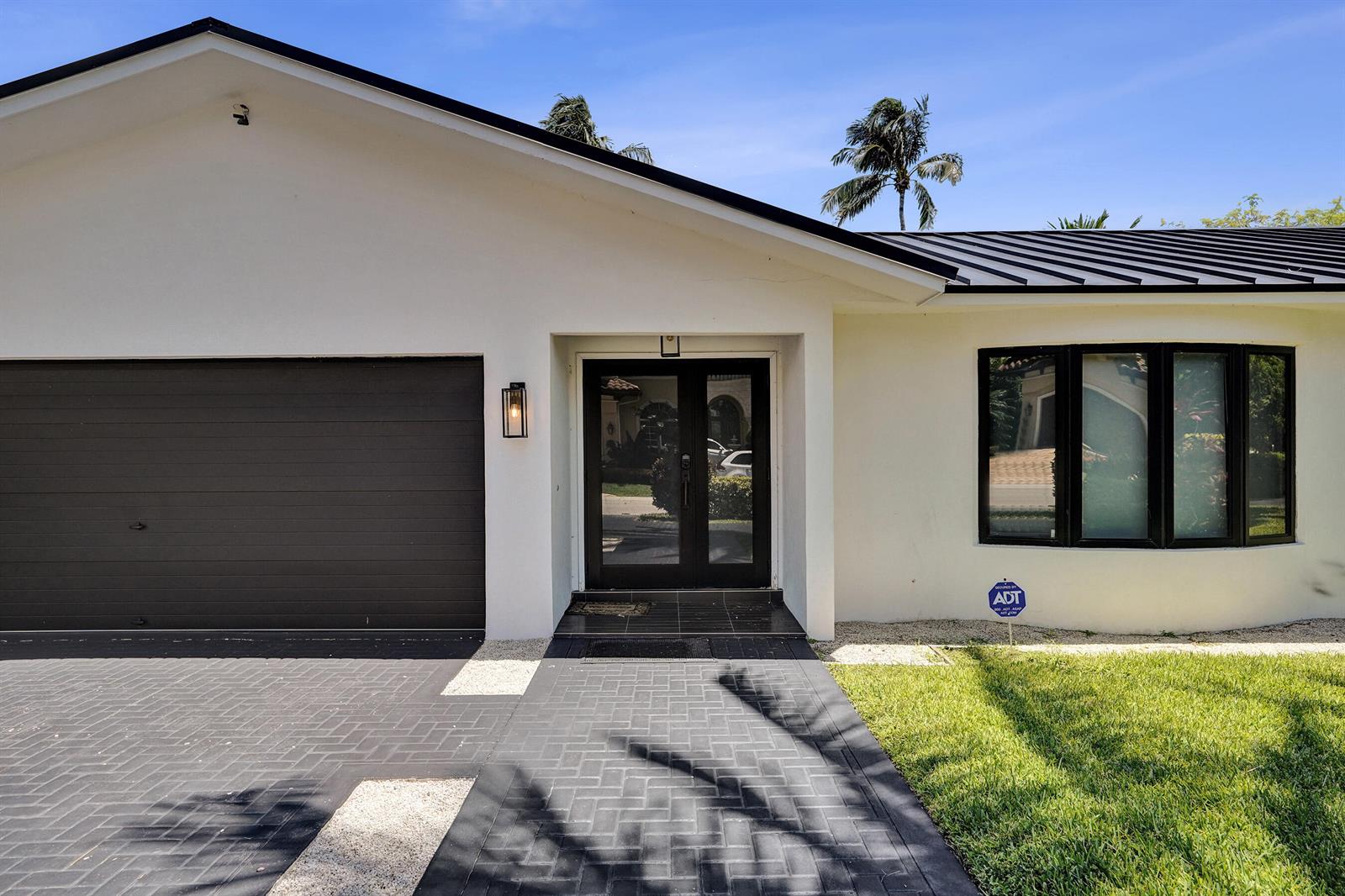 A white house exterior features a dark garage door, a glass front door, and a bay window — 933 Banyan Drive, Delray Beach FL 33483, DELRAY BEACH, FL