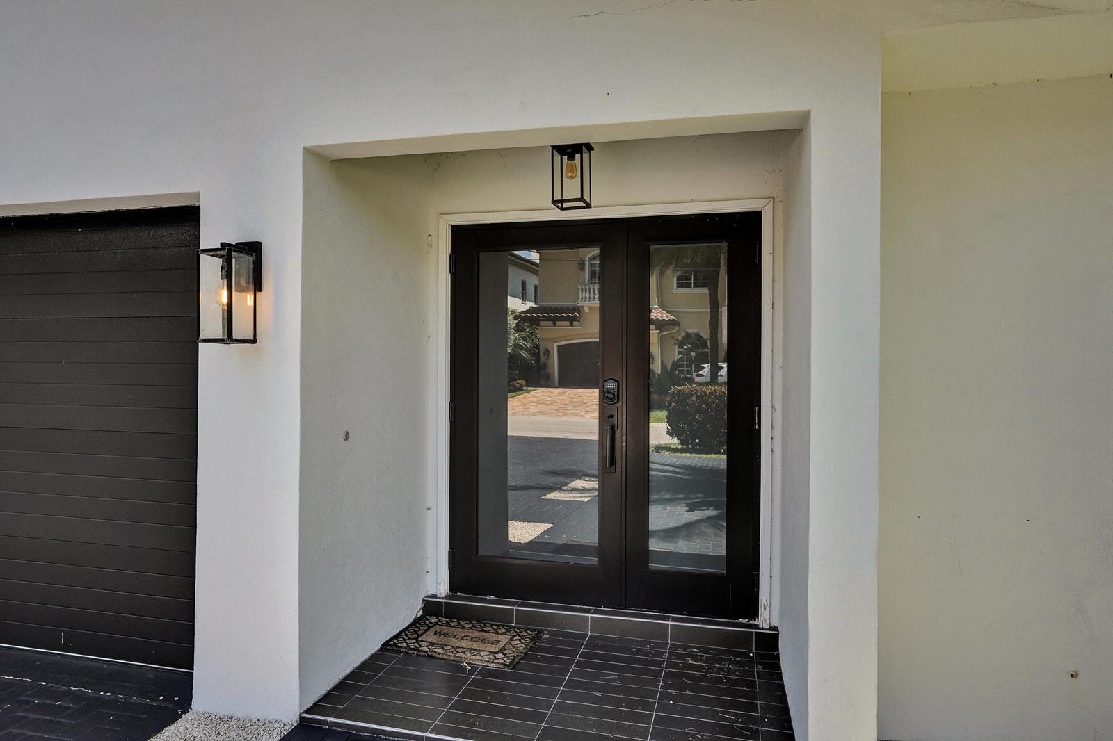 A dark-framed double glass door sits under a recessed entryway with two wall-mounted lanterns — 933 Banyan Drive, Delray Beach FL 33483, DELRAY BEACH, FL