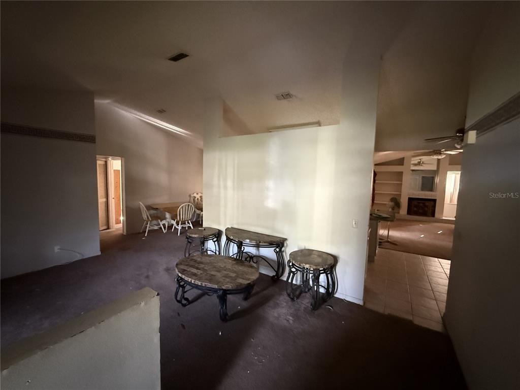 A living area with carpeted floors, a partial wall, and a view into a dining room — 1231 GAGE AVENUE, DELTONA, FL