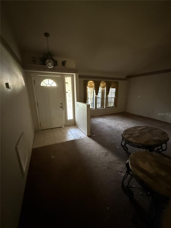 A living room with brown carpet, a front door, and two round wooden tables — 1231 GAGE AVENUE, DELTONA, FL