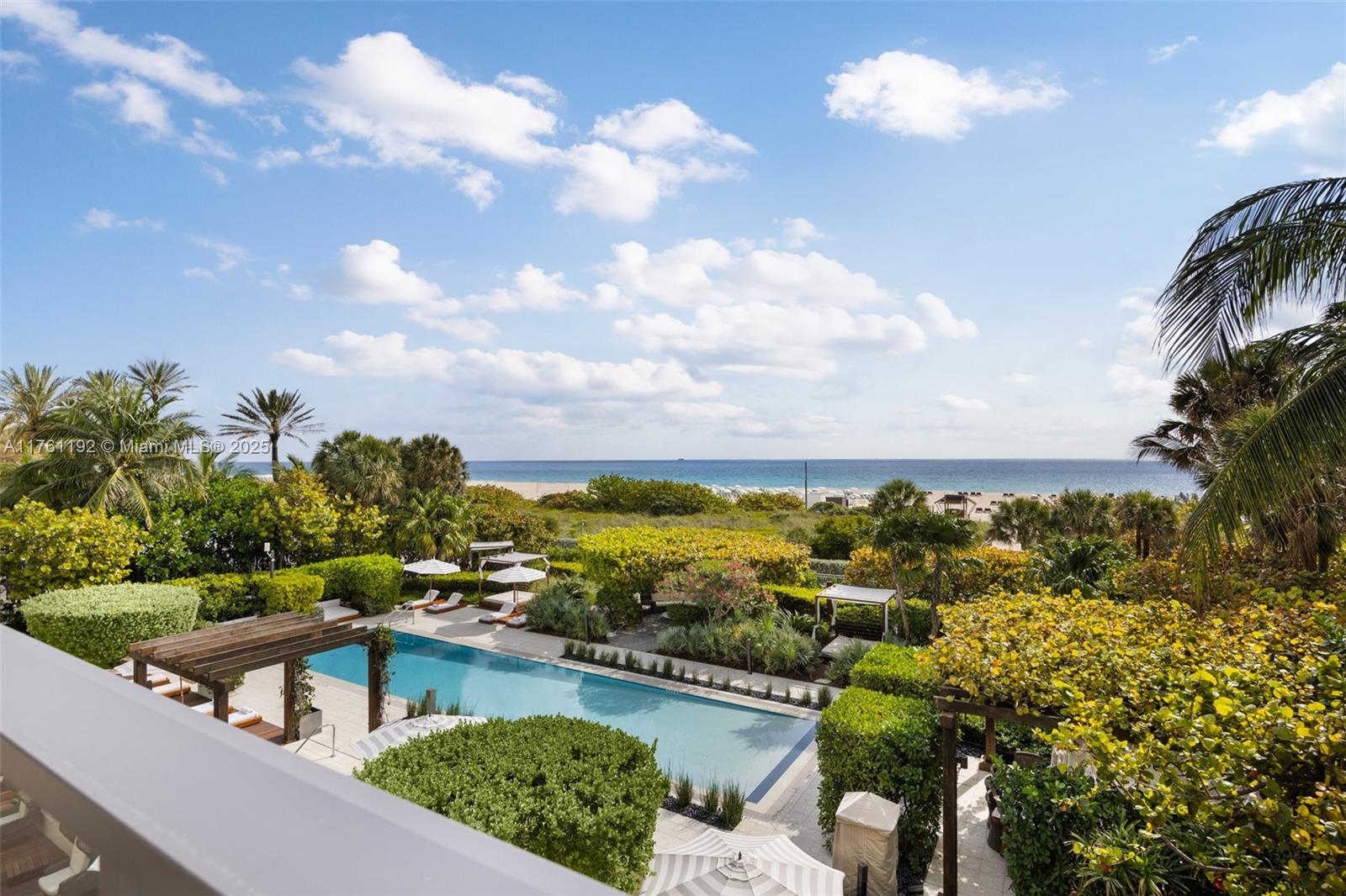 An elevated view of a swimming pool surrounded by lush landscaping and the ocean beyond — 125 Ocean Dr # 0303, Miami Beach FL 33139, MIAMI BEACH, FL