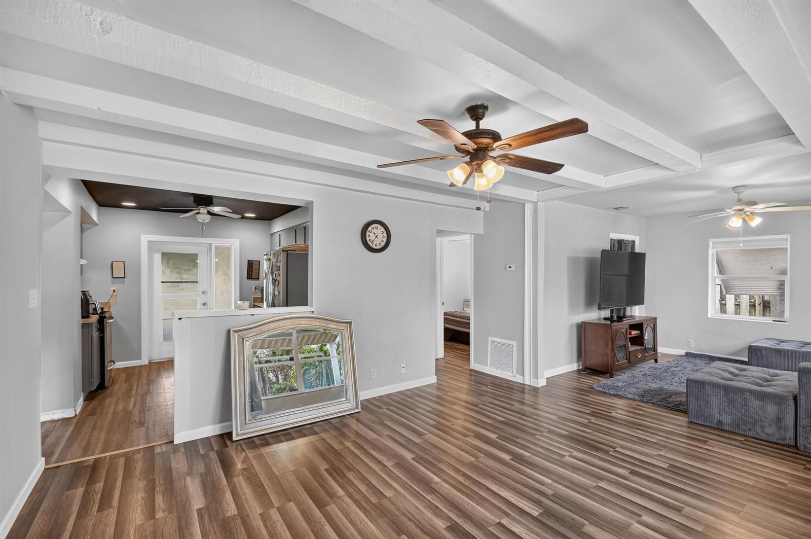 A living room with wood-look flooring, exposed ceiling beams, a ceiling fan, and an adjacent kitchen — 512 SE 1st Street, Boynton Beach FL 33435, BOYNTON BEACH, FL