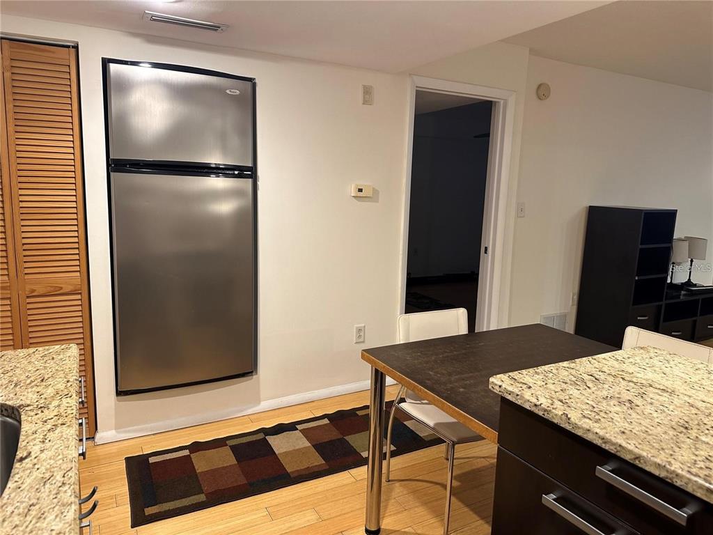 A kitchen area features a stainless steel refrigerator, a dining table, and granite countertops — 701 S MADISON AVENUE UNIT 410, CLEARWATER, FL