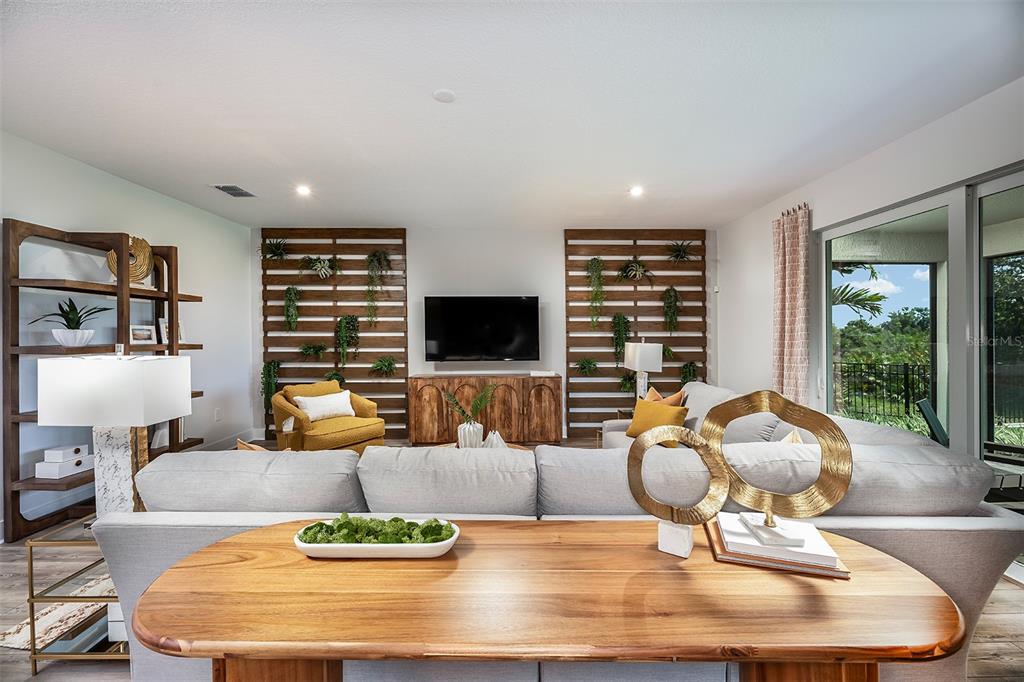 A living room features a sectional sofa, wood-slat accent walls with plants, and a television — 18607 ARBOR VISTA DRIVE, VENICE, FL