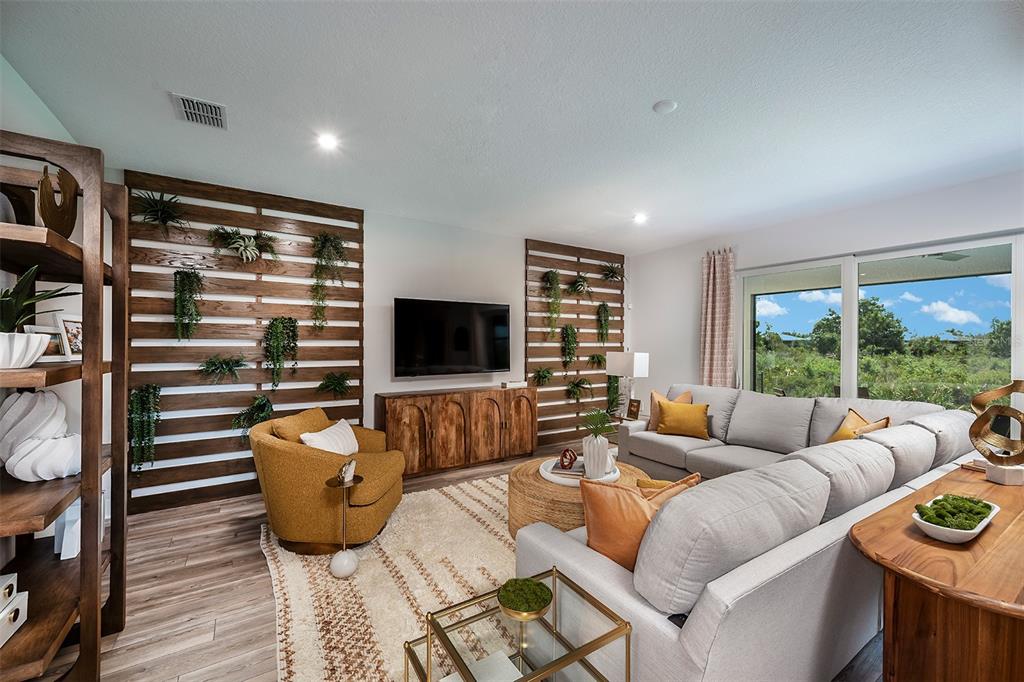 A living room features wood-slat accent walls with hanging plants, a sectional sofa, and furniture — 18607 ARBOR VISTA DRIVE, VENICE, FL