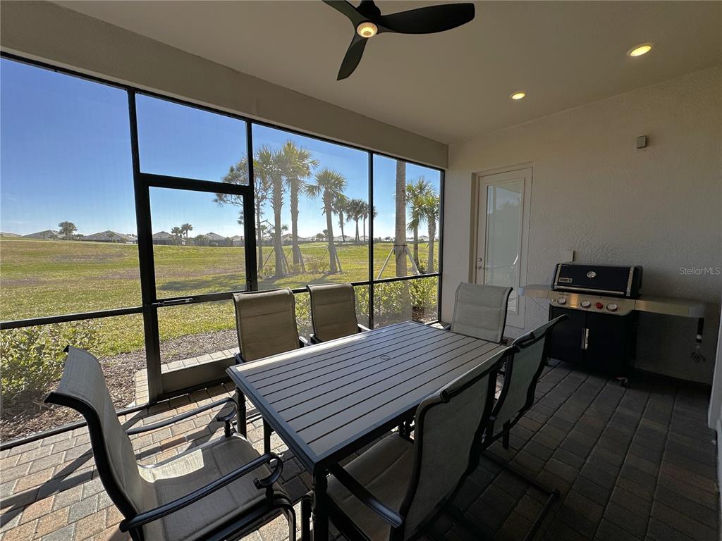 A screened-in patio features a dining set, a grill, and a view of a grassy field — 25115 LONGMEADOW DRIVE, PUNTA GORDA, FL