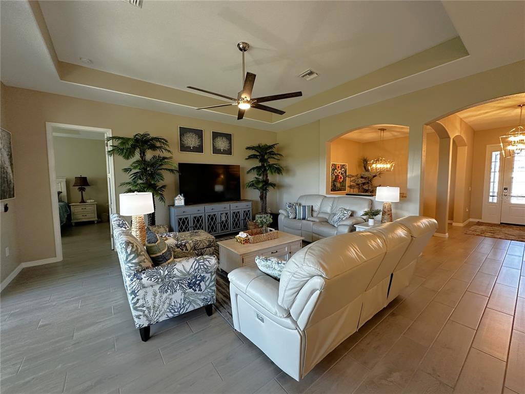 A living room features a tray ceiling, light tile flooring, and a neutral color palette — 25115 LONGMEADOW DRIVE, PUNTA GORDA, FL