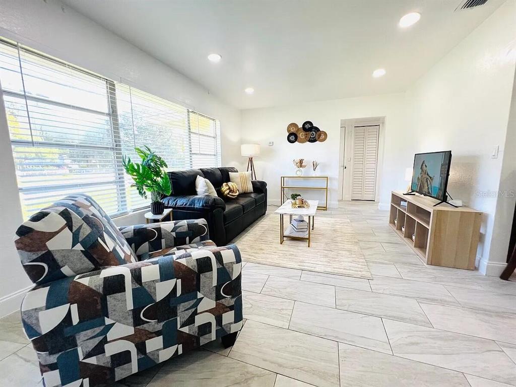A living room features a patterned armchair, a black sofa, and light-colored tile flooring — 1169 DREW STREET, CLEARWATER, FL