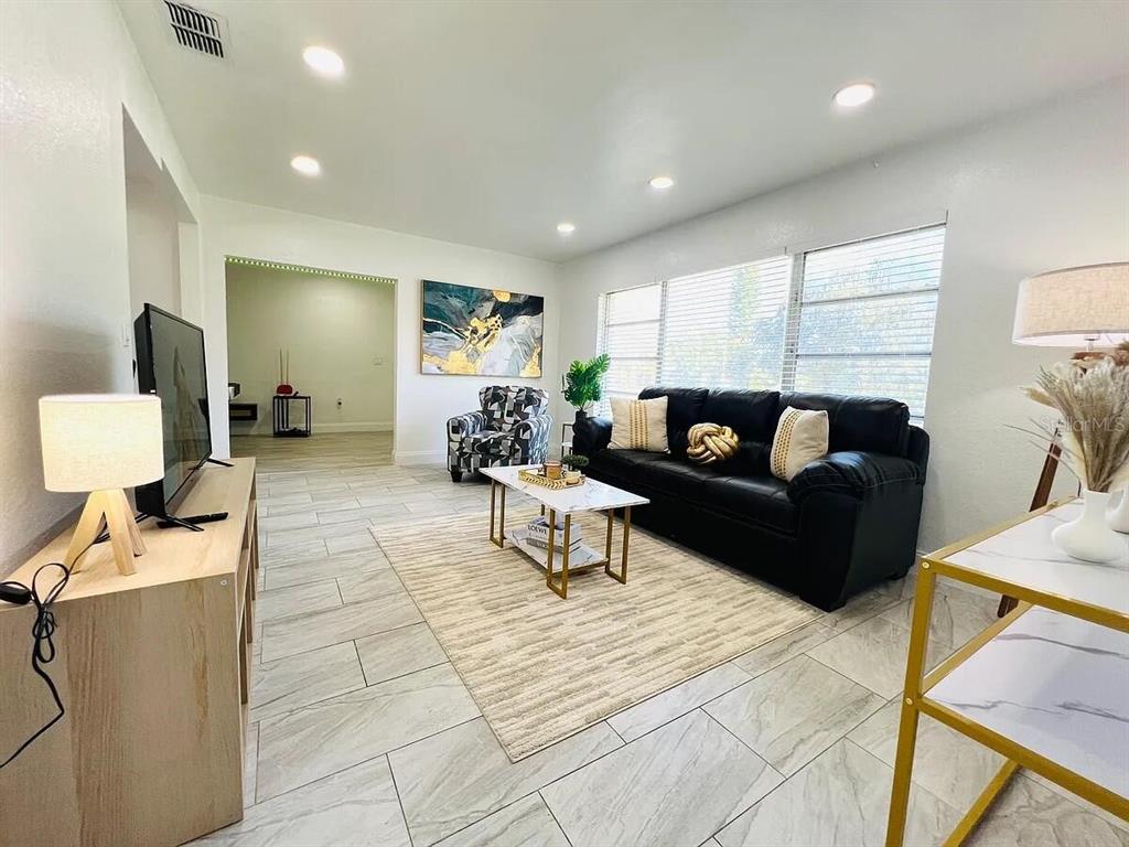 A living room features a black leather sofa, patterned armchair, and light-colored tile flooring — 1169 DREW STREET, CLEARWATER, FL