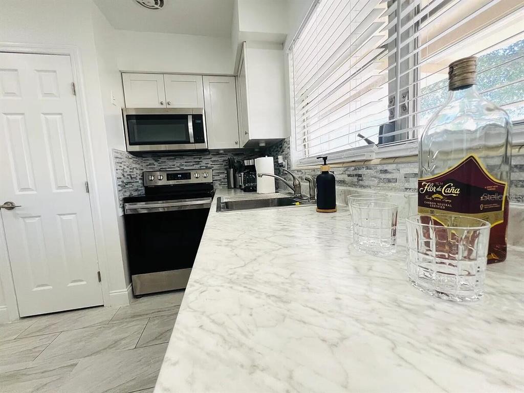 A kitchen features white cabinets, a marble-patterned countertop, stainless steel appliances, and a tile backsplash — 1169 DREW STREET, CLEARWATER, FL