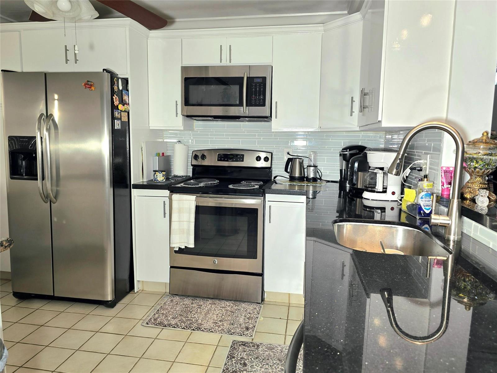 A kitchen features white cabinets, stainless steel appliances, black countertops, and light tile flooring — 2002 Granada Drive # K3, Coconut Creek FL 33066, COCONUT CREEK, FL